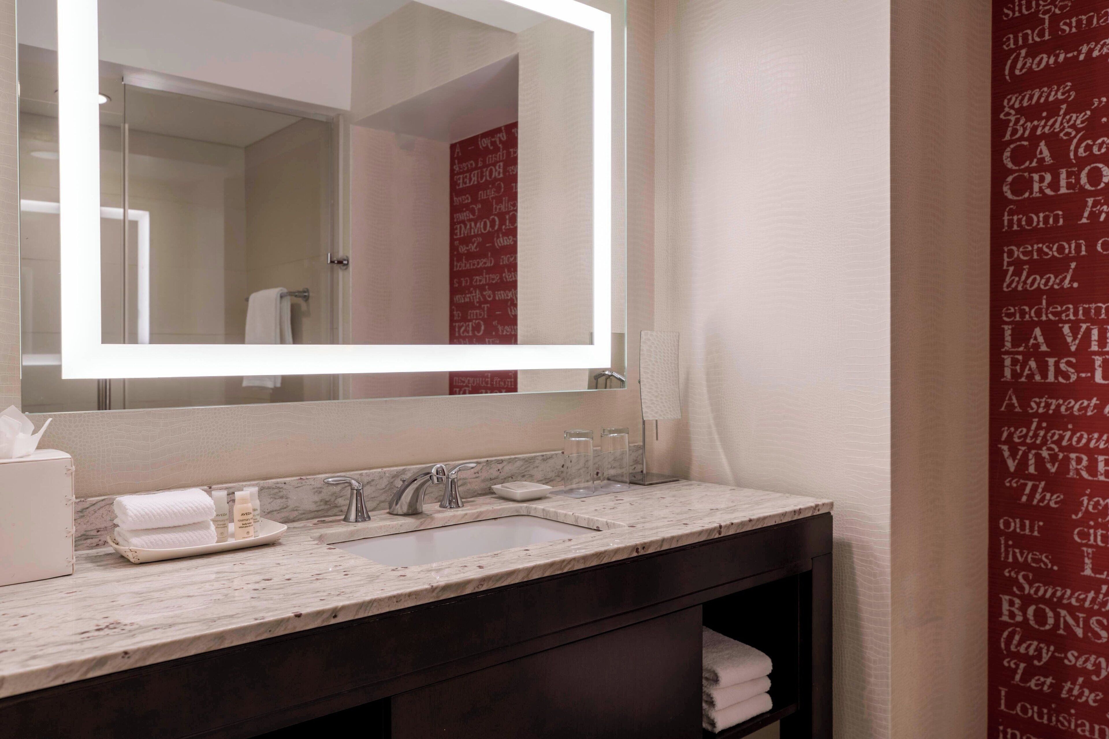 Un baño con un espejo grande, un lavabo y un mueble de tocador con un armario oscuro. Hay toallas y artículos de aseo en la encimera.