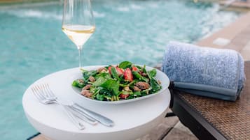 Una mesa de comedor con una ensalada, una copa de vino blanco y una toalla al lado de una piscina.
