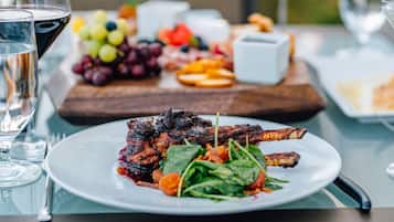 Uma mesa de jantar com um prato de carne grelhada, um copo de vinho tinto e uma seleção de frutas e legumes.