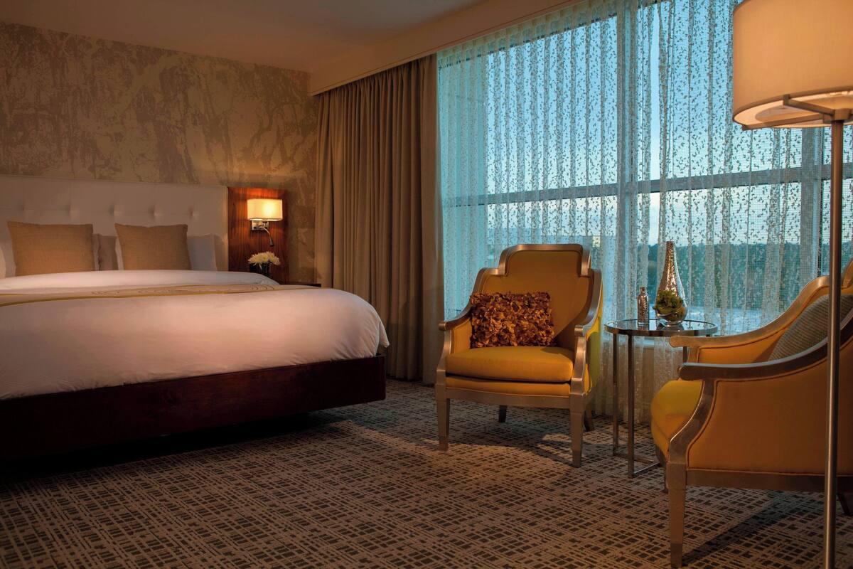 A hotel room with a large bed, a chair, a small table, and a lamp.