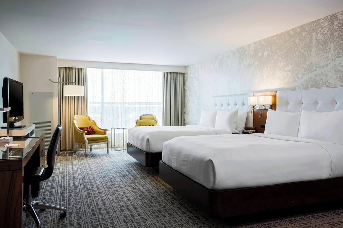 A hotel room with two beds, a desk with a television, a chair, and a small table.