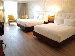 Une chambre d’hôtel avec deux lits, un bureau, une chaise et une lampe.
