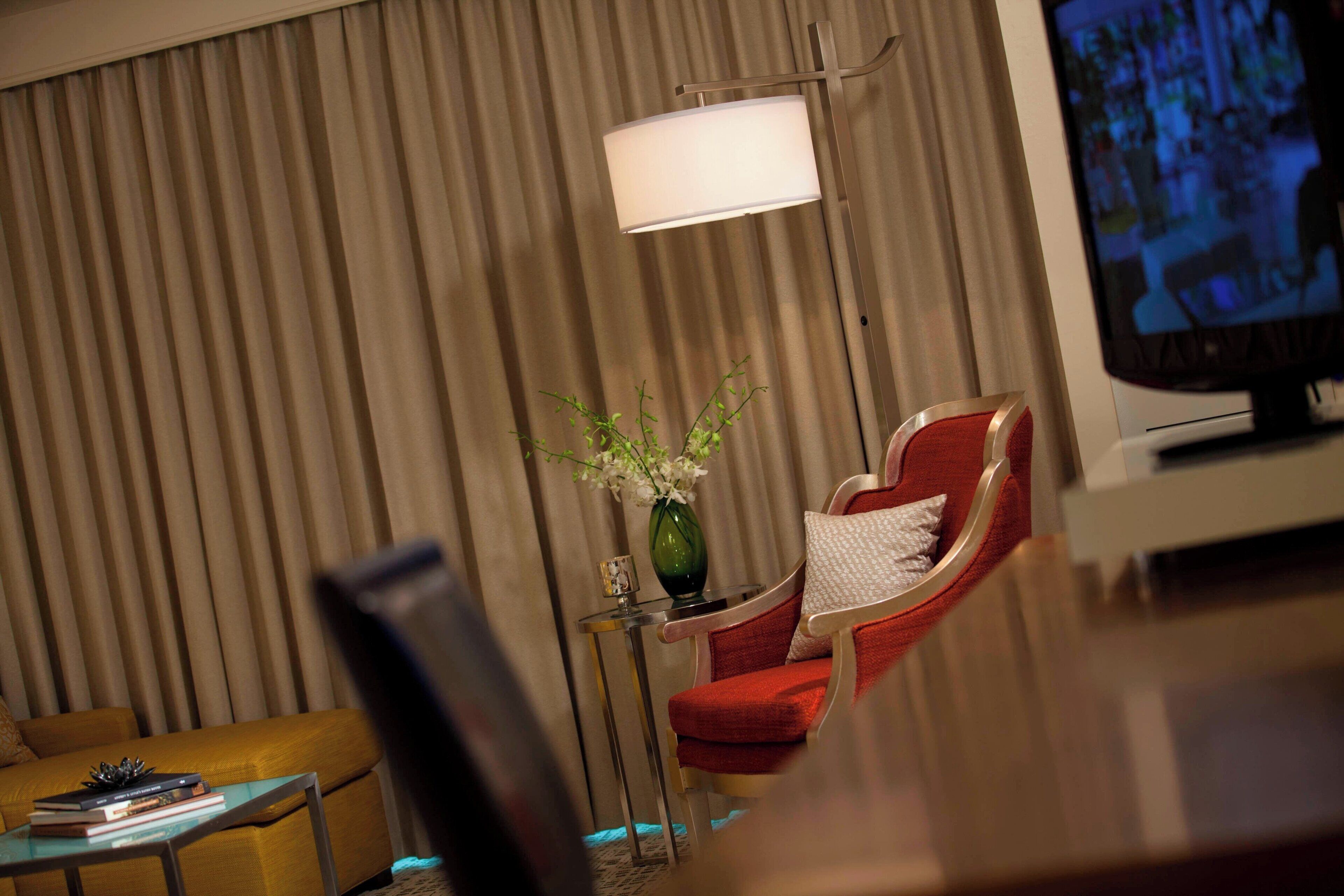 A modern living room with a sofa, a red armchair, a small table with a vase, and a television.