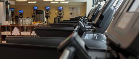 A row of stationary treadmills in a gym with exercise equipment and TVs in the background.