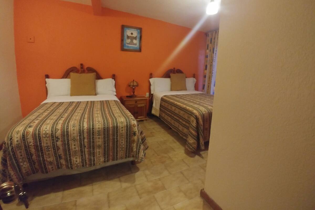 Habitación con dos camas, cada una con ropa de cama estampada, una mesita y un cuadro en la pared.