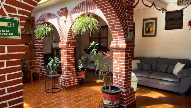 Un hall d’entrée avec des arches en briques, des plantes en pot, un canapé et un panneau indiquant une voie d’évacuation.