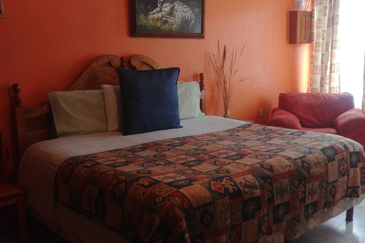Un dormitorio con cama, una silla roja, cabecero de madera y un cuadro en la pared.