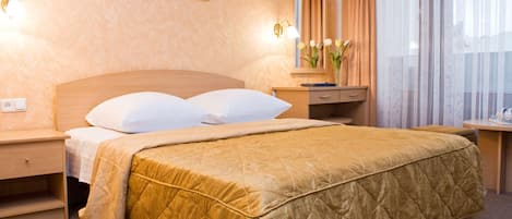 A hotel room with a large bed, a nightstand, a desk, a mirror, and a window with curtains.