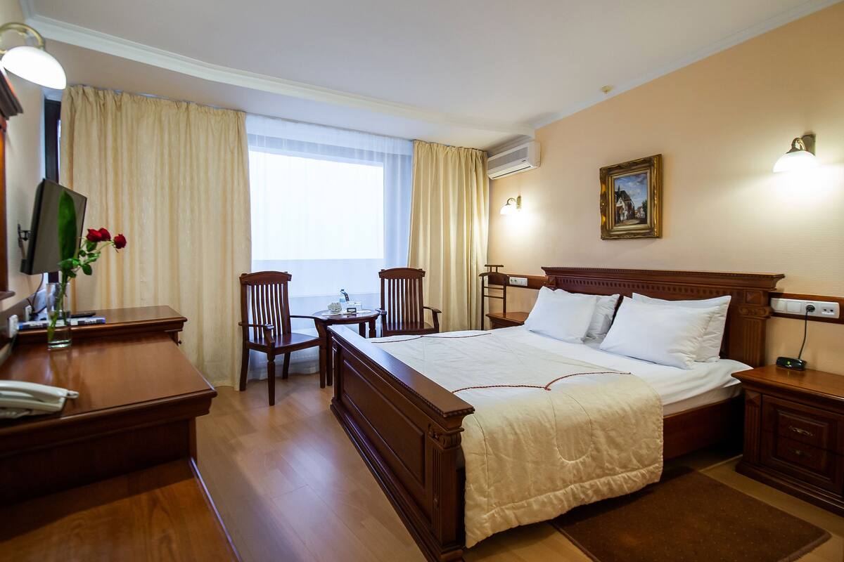 A hotel room with a large bed, a desk, a chair, and a TV.