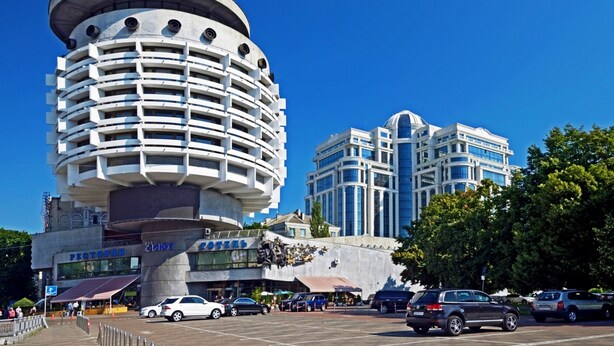 Un bâtiment moderne à la base cylindrique, doté de nombreux balcons et entouré d’autres constructions contemporaines.