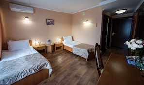 A hotel room with two beds, a wooden floor, a desk with a vase of flowers, and a picture on the wall. - Hotel Salute (Kyiv)