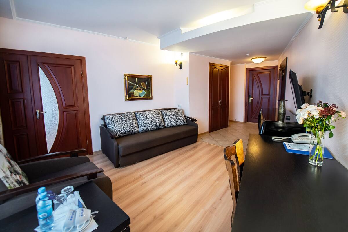 A modern living room with a sofa, a dining table with a vase of flowers, and a wooden floor.