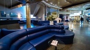Un hall d'entrée moderne avec des espaces de détente bleus, un comptoir d'accueil et un escalier menant aux étages supérieurs.