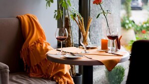 Un coin repas chaleureux avec une table dressée pour deux, agrémentée de verres à vin, d’une bougie et d’un vase contenant une rose.