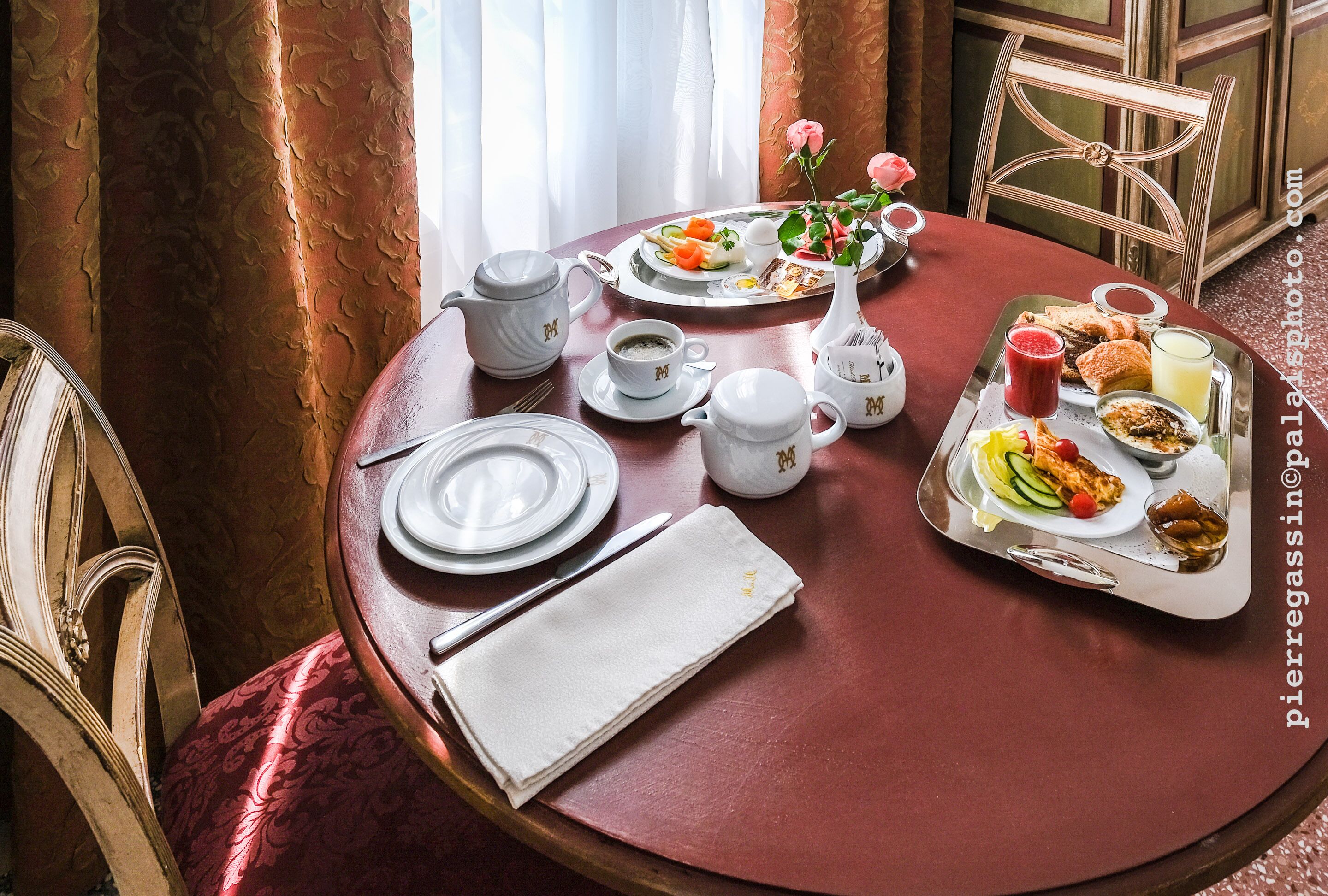 A dining table set with plates, cutlery, a teapot, a pitcher, and a tray with food and drinks.