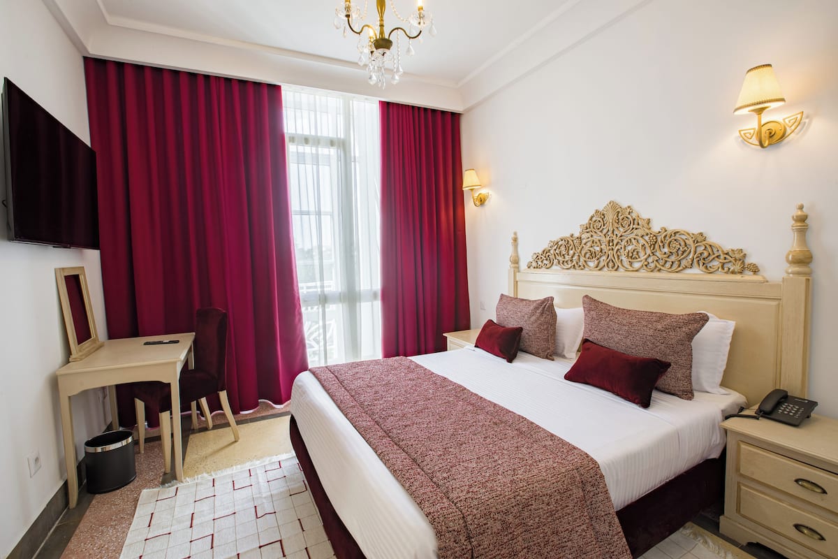 A hotel room with a large bed, a desk, a chair, a TV, and a chandelier.