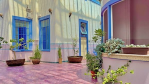 Un cortile con piante in vaso, pavimento piastrellato e un edificio con finestre a cornice blu e facciata bianca.