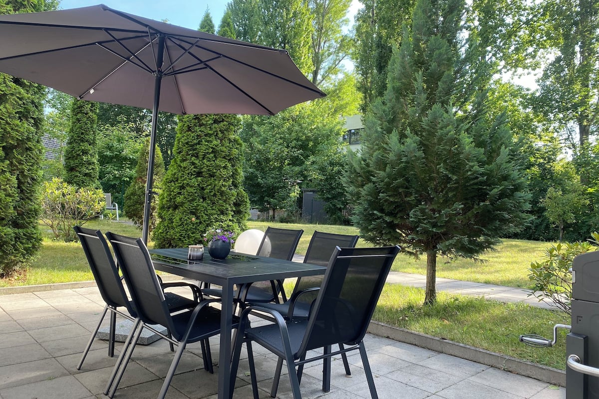 Eine Terrasse im Freien mit Tisch, Stühlen, einem großen Sonnenschirm und einem Grill.
