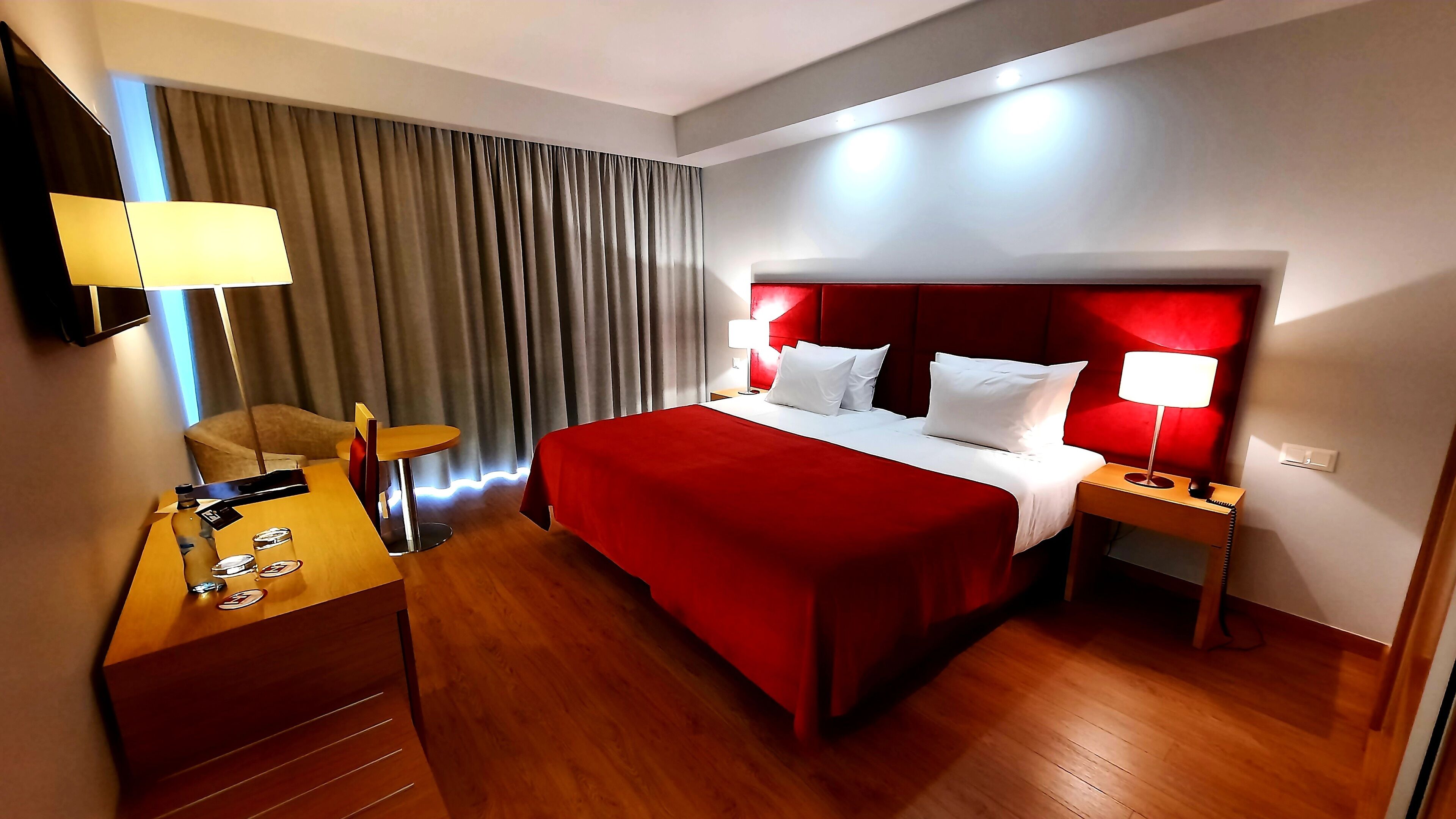 Een hotelkamer met een groot bed, een bureau, een stoel, een nachtkastje, een lamp en een televisie.