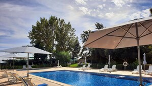 A swimming pool with lounge chairs and umbrellas, surrounded by trees and a gazebo. - BejaParque Hotel (Beja)