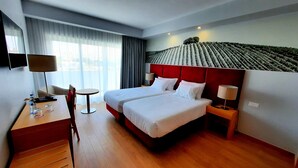 A hotel room with two beds, a desk, a chair, a table, and a TV. - BejaParque Hotel (Beja)