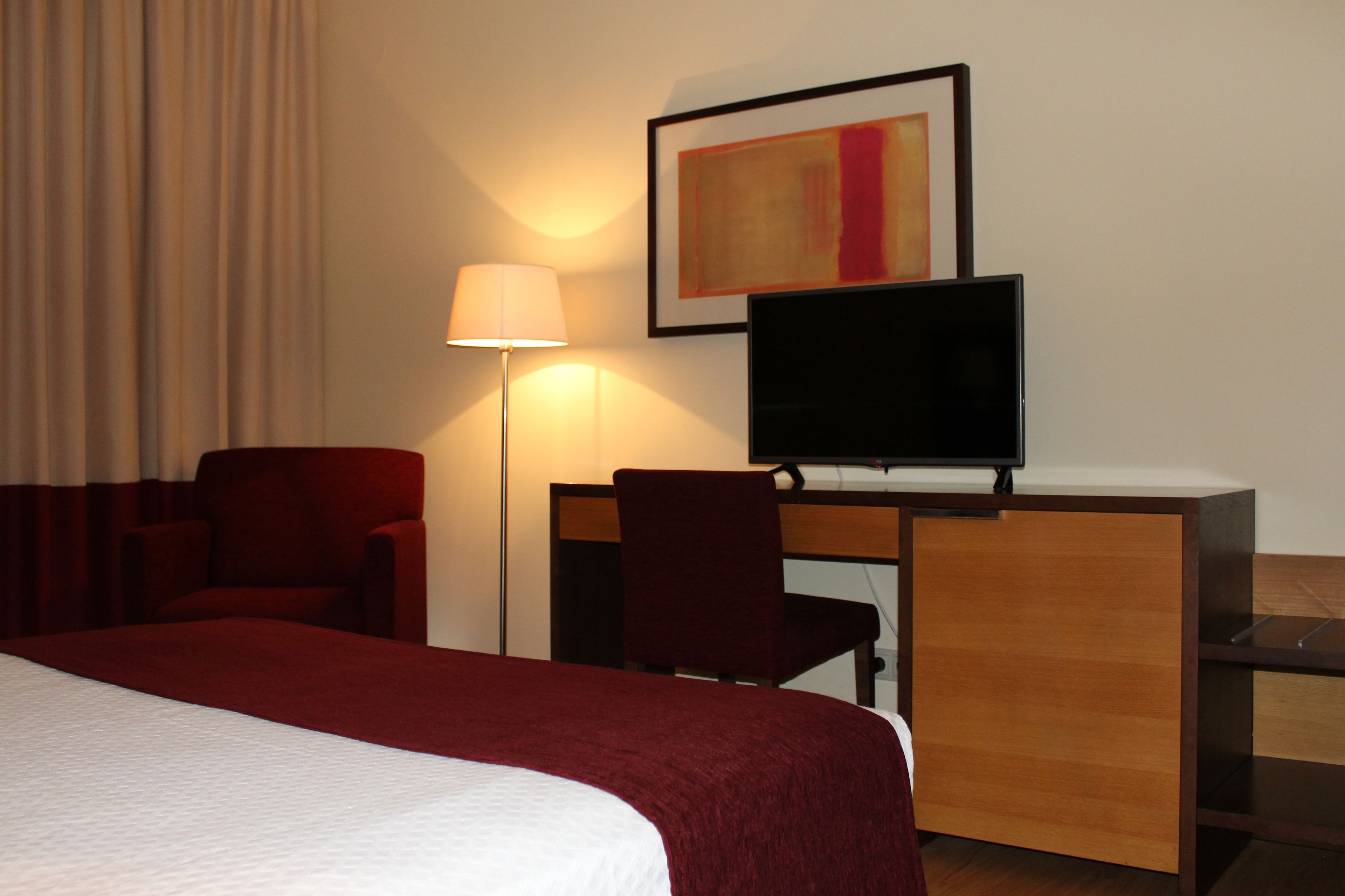 A hotel room with a bed, a desk, a chair, a television, and a lamp.