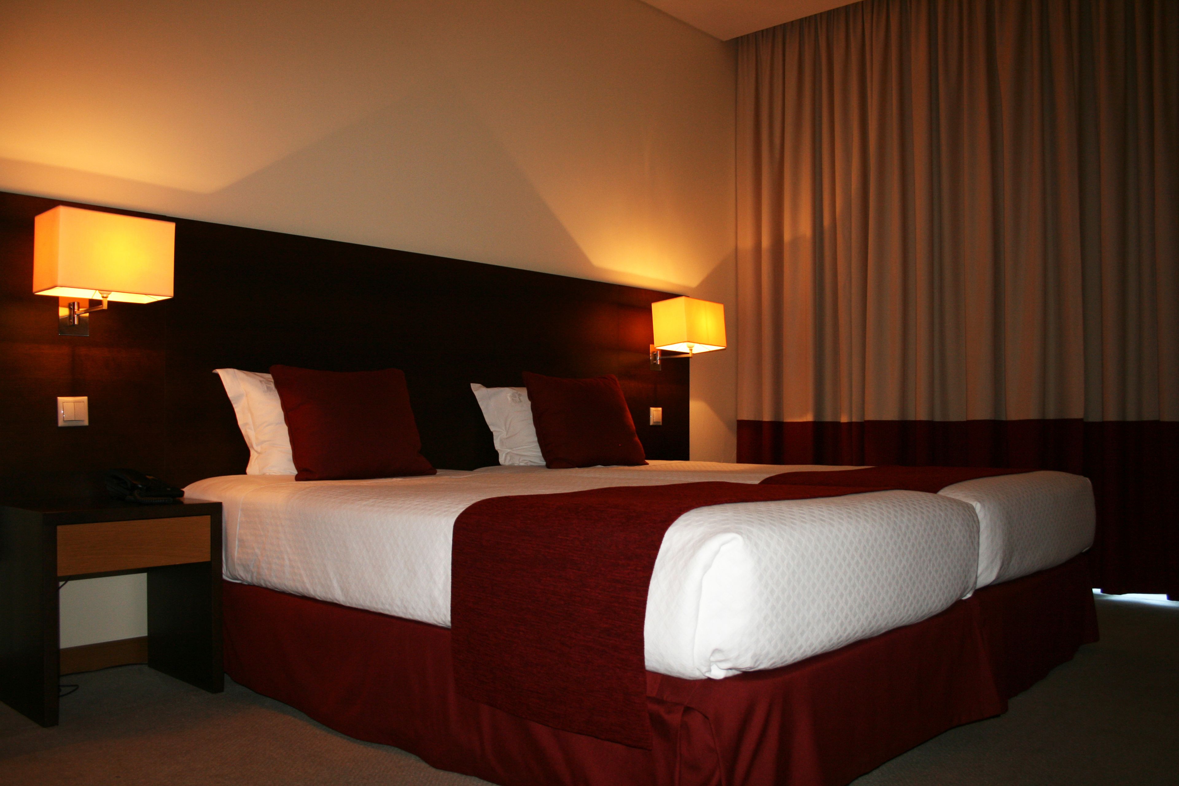 A hotel room with a large bed, two bedside lamps, a nightstand, and a curtain.
