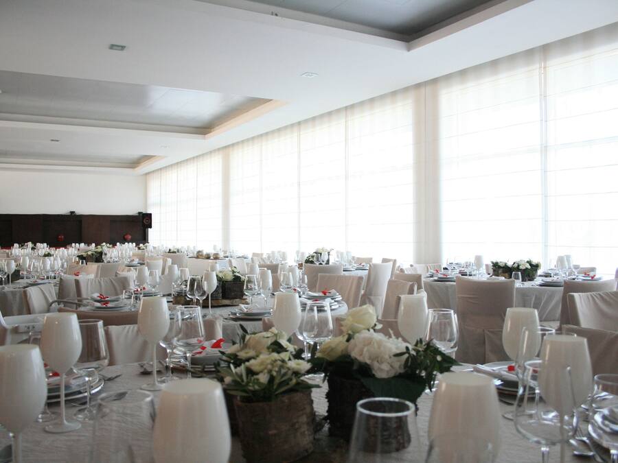 A banquet hall with round tables set for a formal event, featuring white tablecloths, chairs, and floral centerpieces.