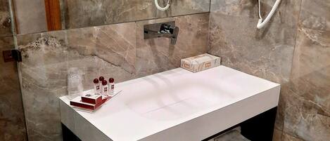 Een badkamer met een witte wastafel, een spiegel, een handdoekhouder en een douche.
