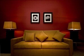 A room with a sofa, two framed pictures on the wall, and two lamps on either side.