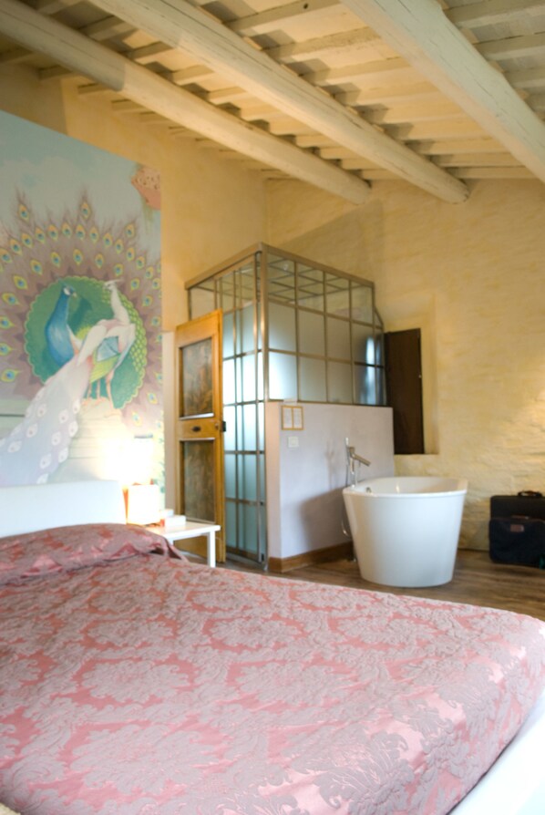 A bedroom with a bed, a large window, and a bathroom with a bathtub.