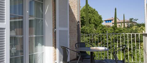 Un balcon avec une table et des chaises, une porte-fenêtre coulissante et une vue sur une maison et des arbres.