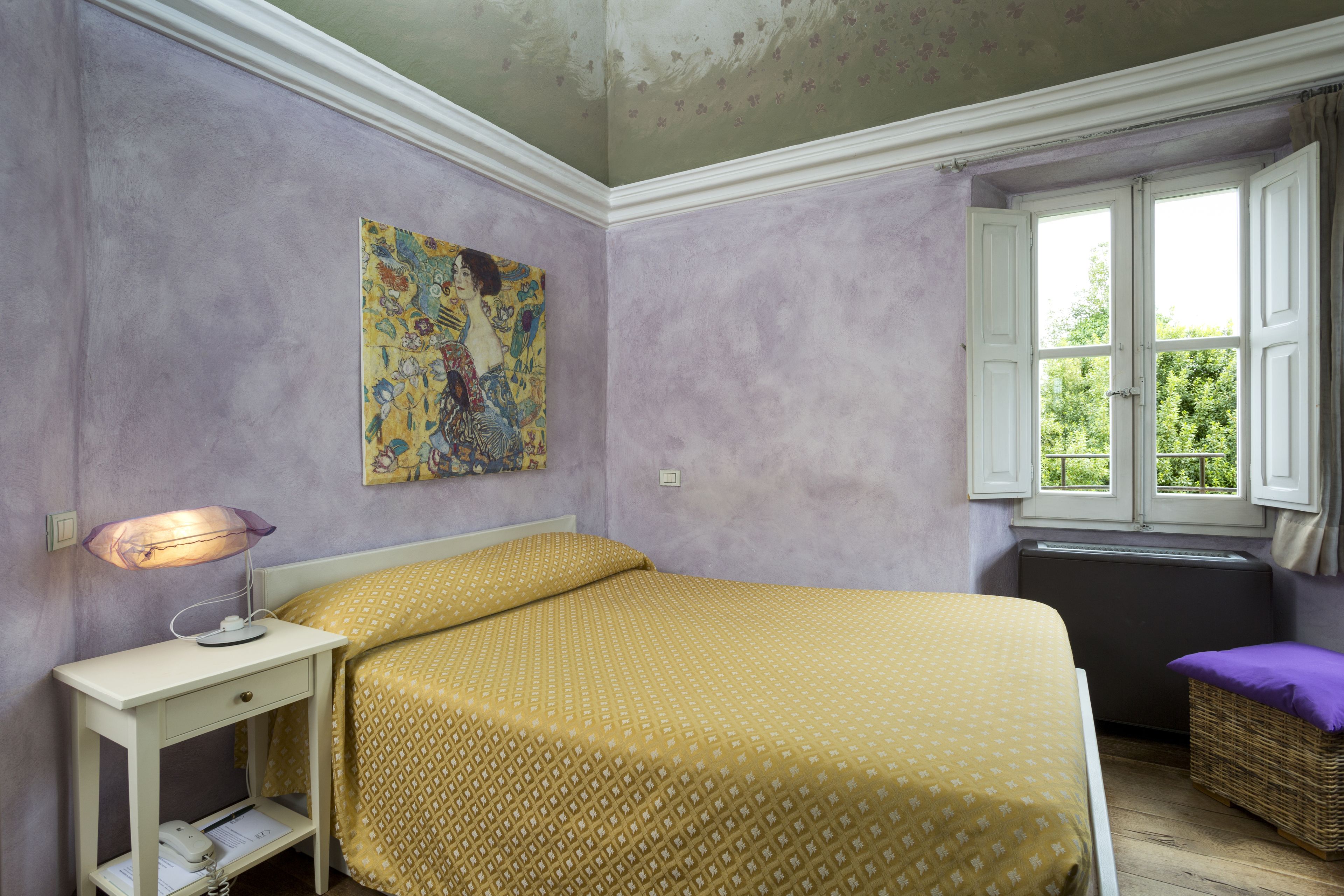 A room with a bed, a nightstand, a lamp, a window with curtains, and a painting on the wall.