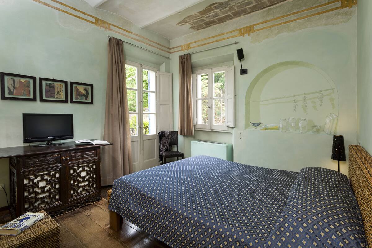 A bedroom with a bed, a television on a dresser, and a window with curtains.