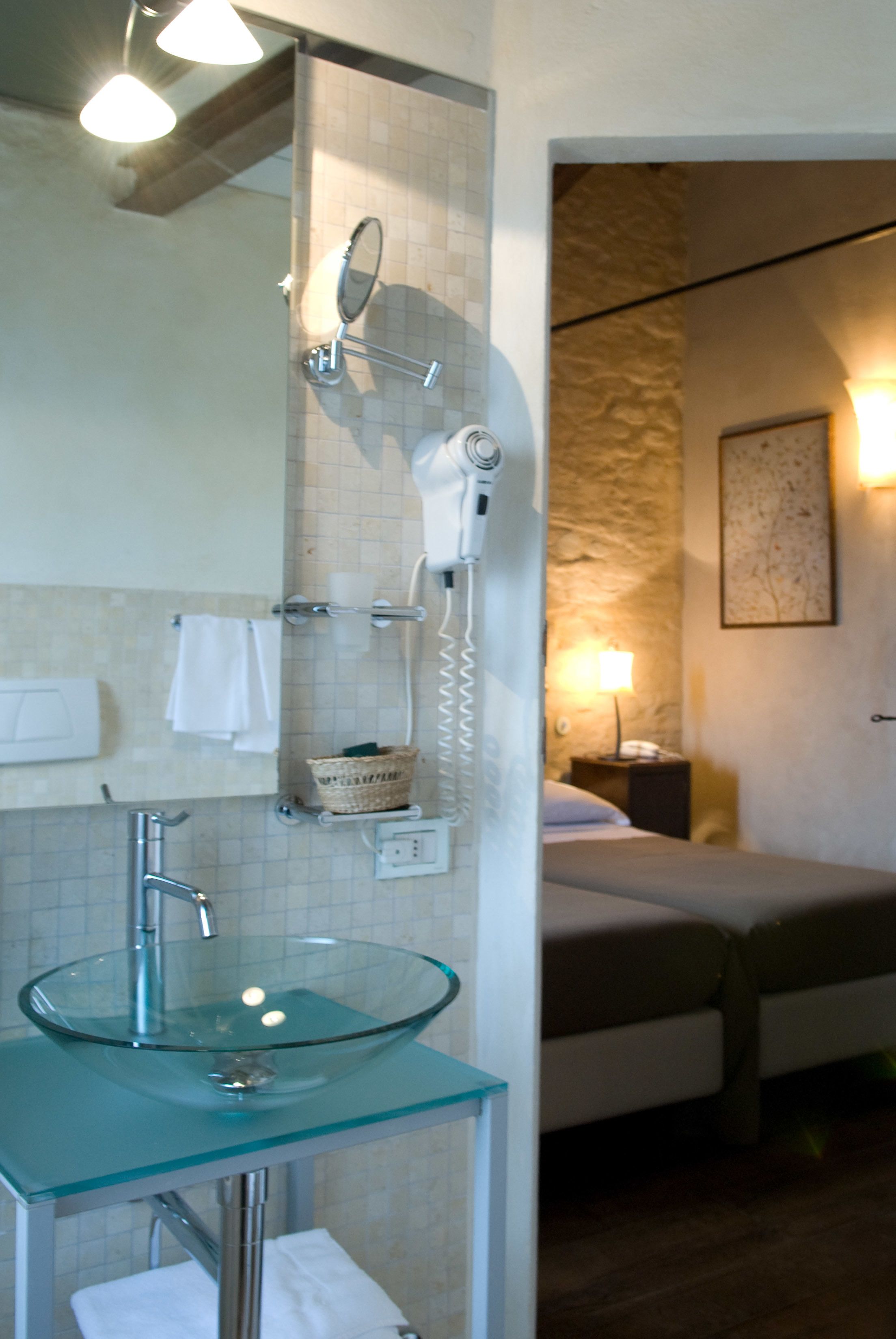 A bathroom with a glass sink, a hairdryer, and a mirror.