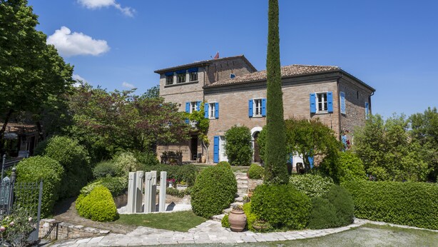 A two-story building with a brick facade, blue shutters, and a well-maintained garden with hedges and a tall cypress tree. - Hotel Il Villino (Santarcangelo di Romagna)