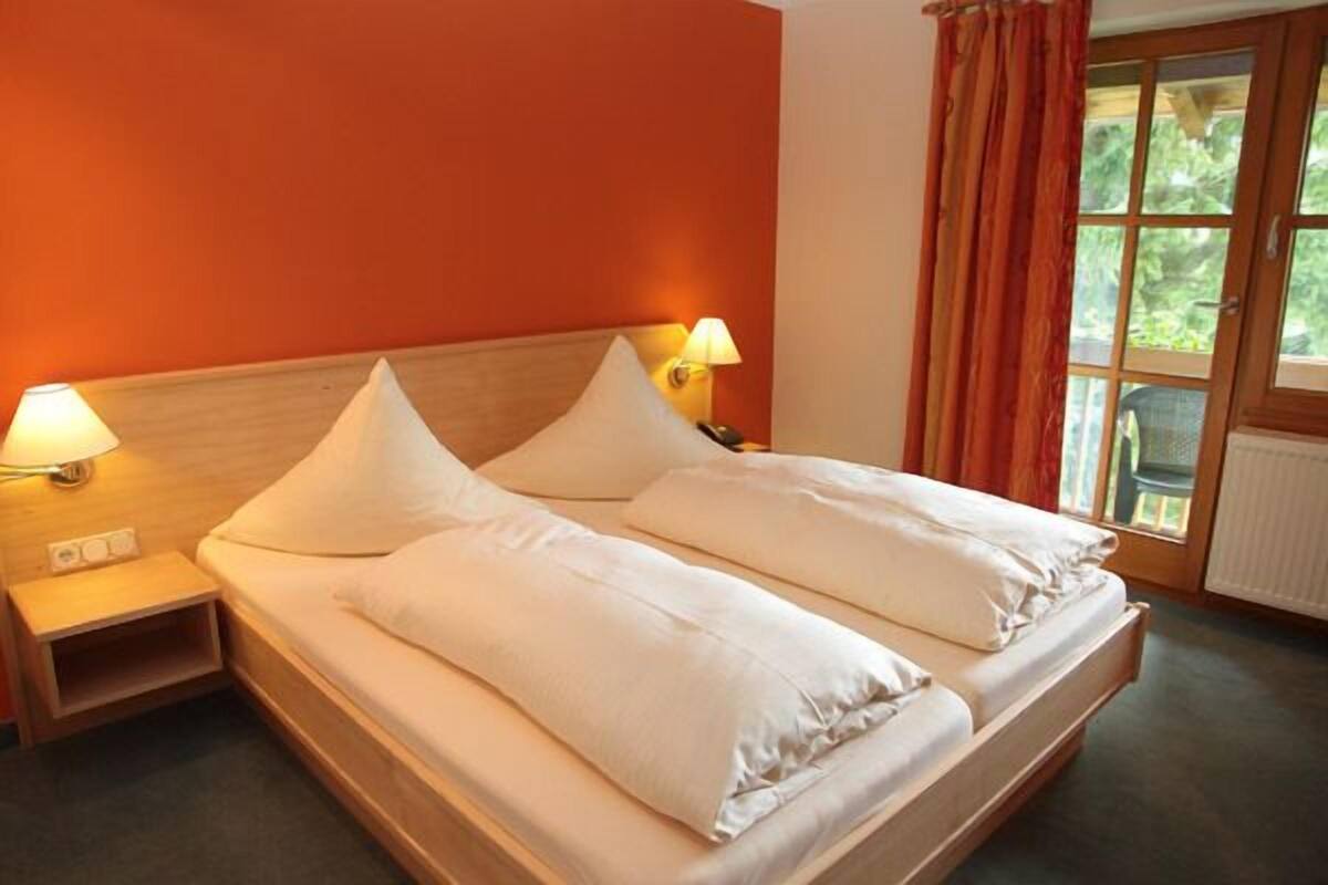 A double bed with white linens, two bedside lamps, and a window with curtains.