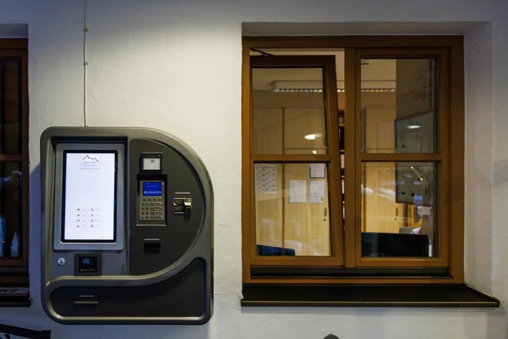 Ein Selbstbedienungskiosk mit Bildschirm und Tastatur, an einer Wand neben einem Fenster mit Holzrahmen befestigt.