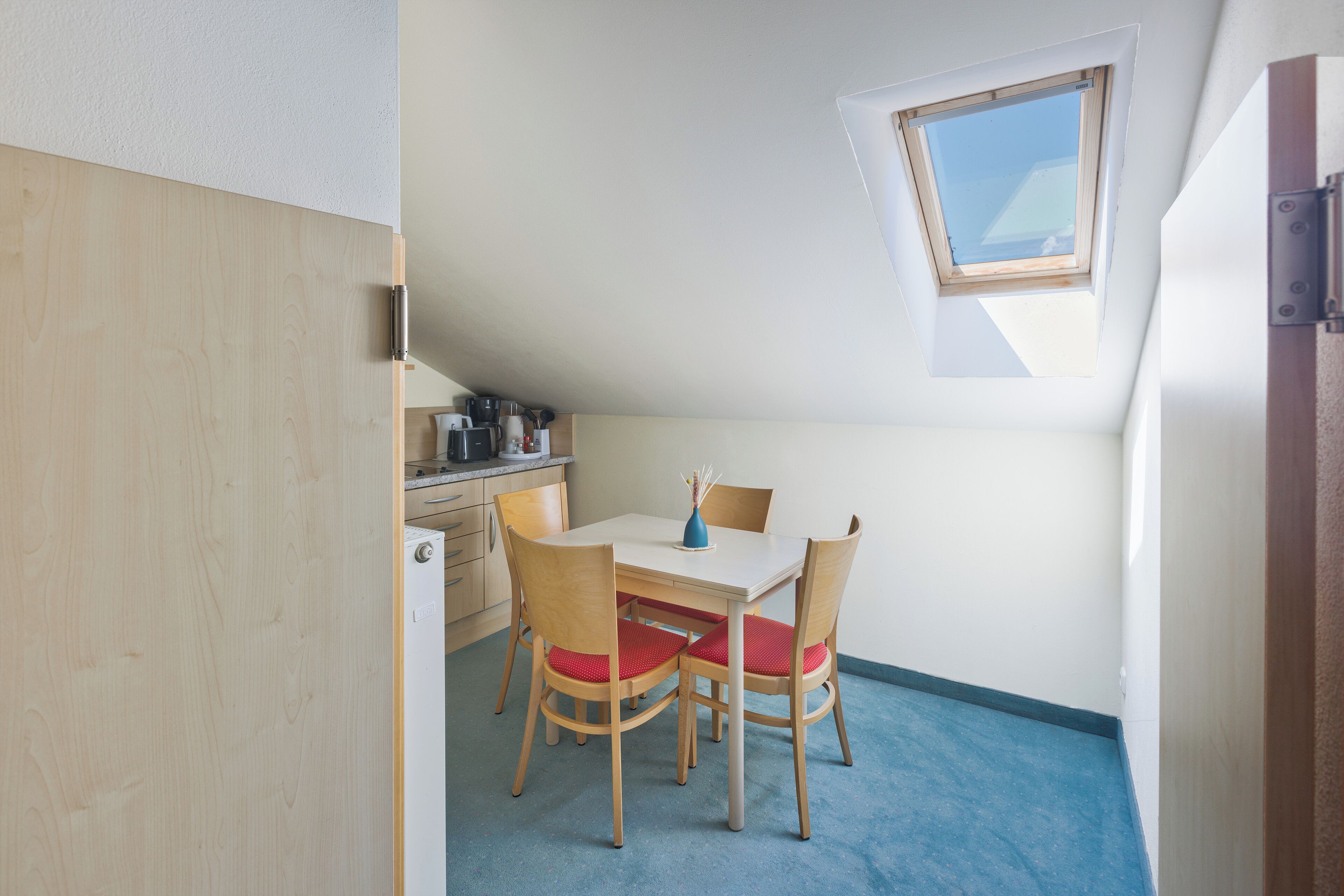 Una habitación pequeña y bien iluminada con una mesa de comedor, sillas, una ventana y una kitchenette.
