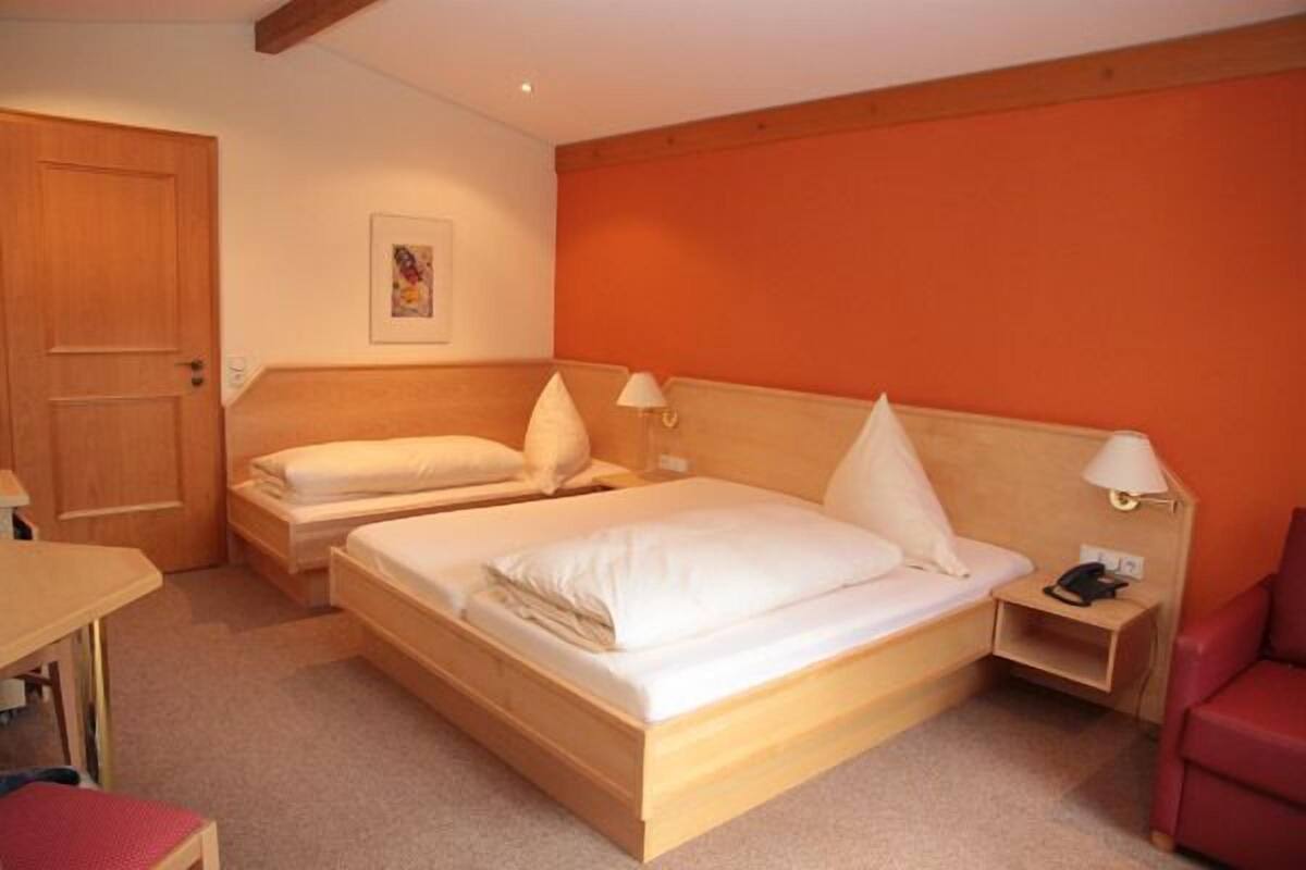 A hotel room with two beds, a desk, a chair, and a nightstand with a lamp.