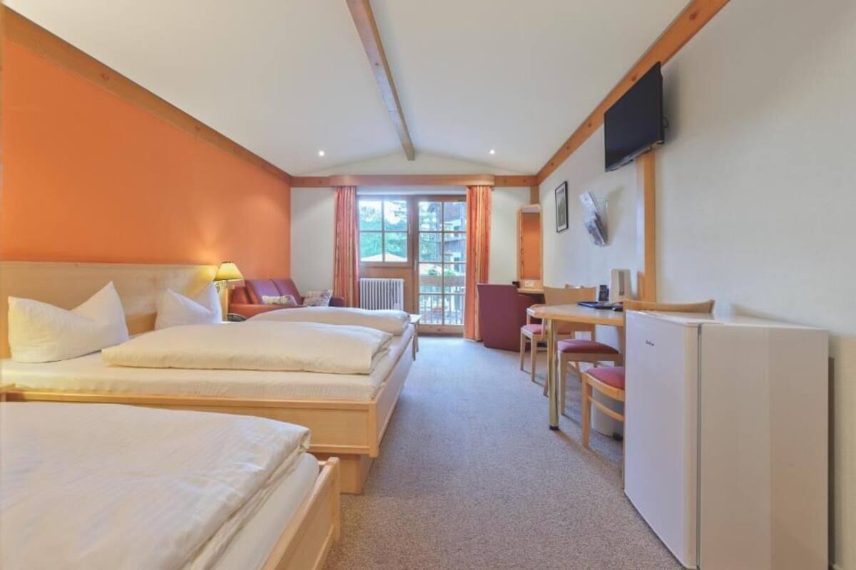 A hotel room with two beds, a desk, a chair, a television, and a window with curtains.