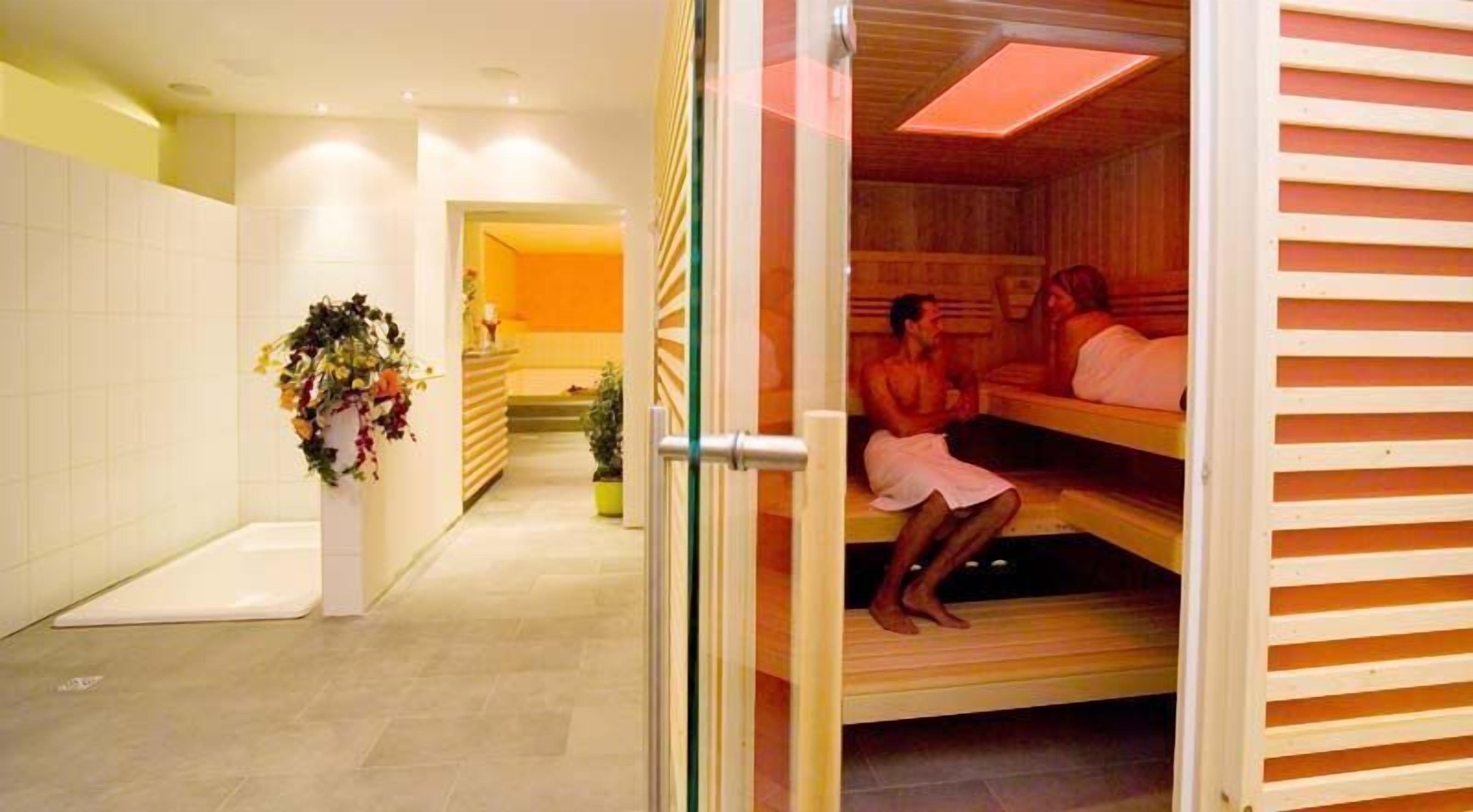 A sauna room with two benches and a door leading to a hallway with a potted plant.