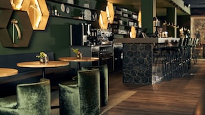 A modern bar area with hexagonal light fixtures, round tables, and cushioned seating.