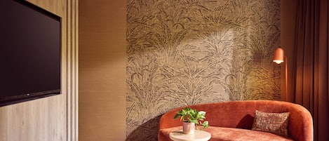 Una sala de estar moderna con un sofá, una mesita redonda con una planta y una pared grande con un diseño de hojas.