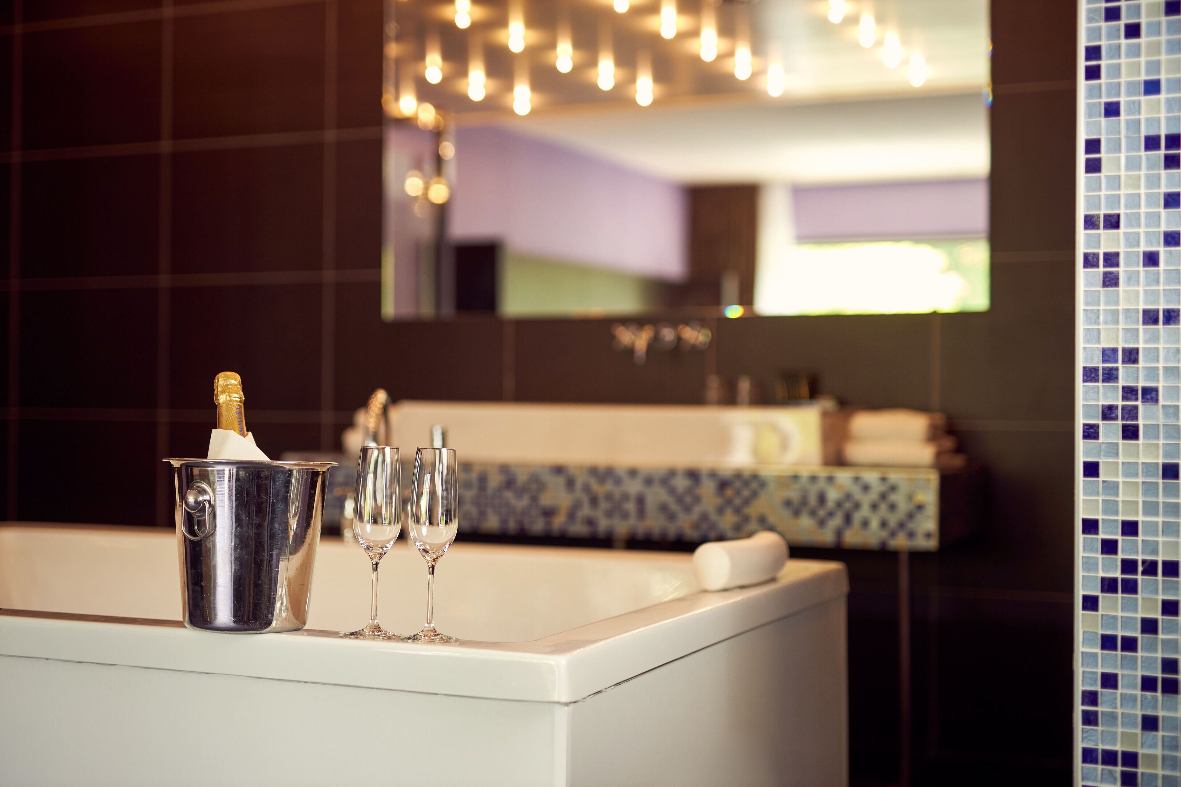 A bathroom with a bathtub, a champagne bottle, and two glasses.