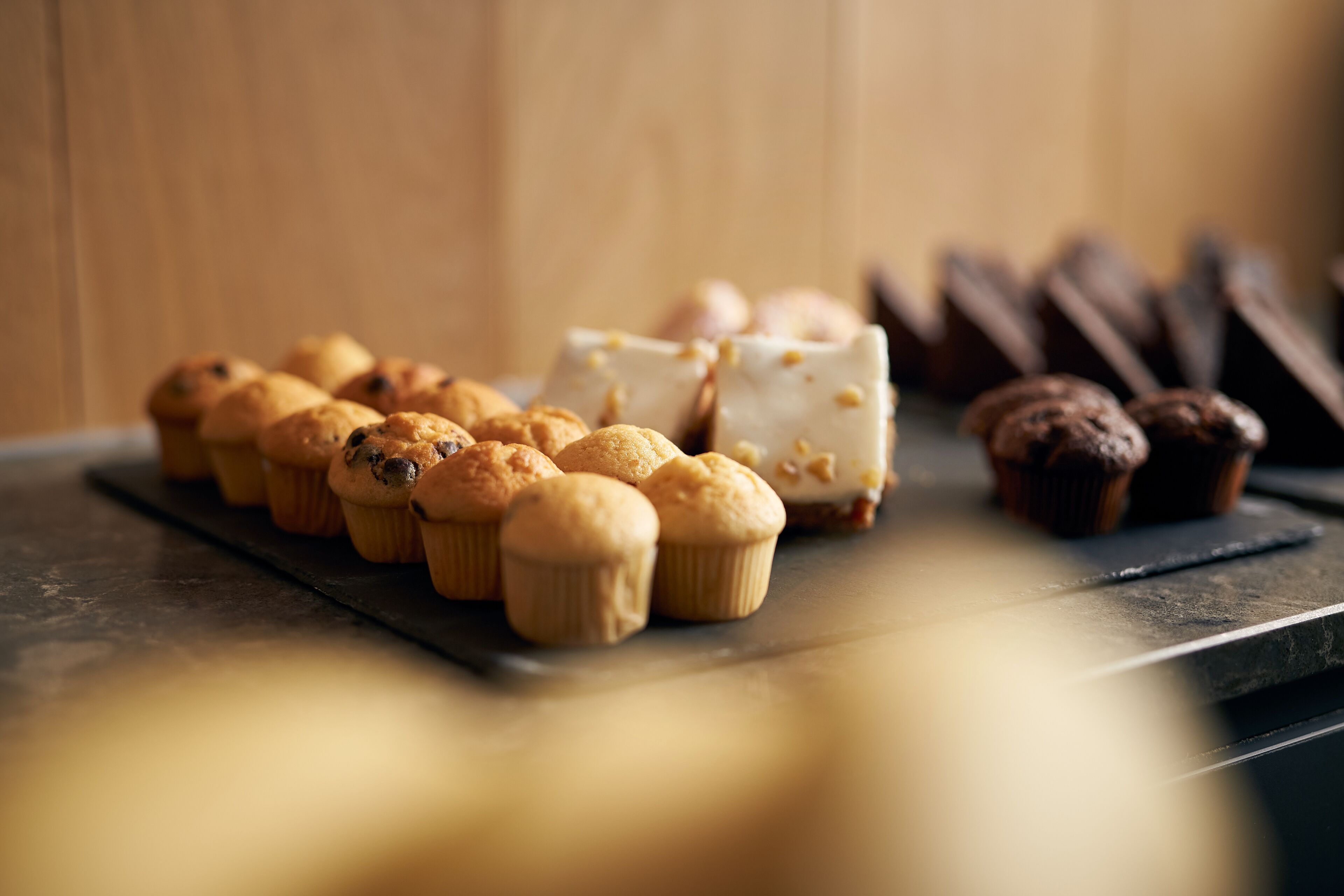 A variety of baked goods on a slate tray, including muffins and a white cake with nuts.