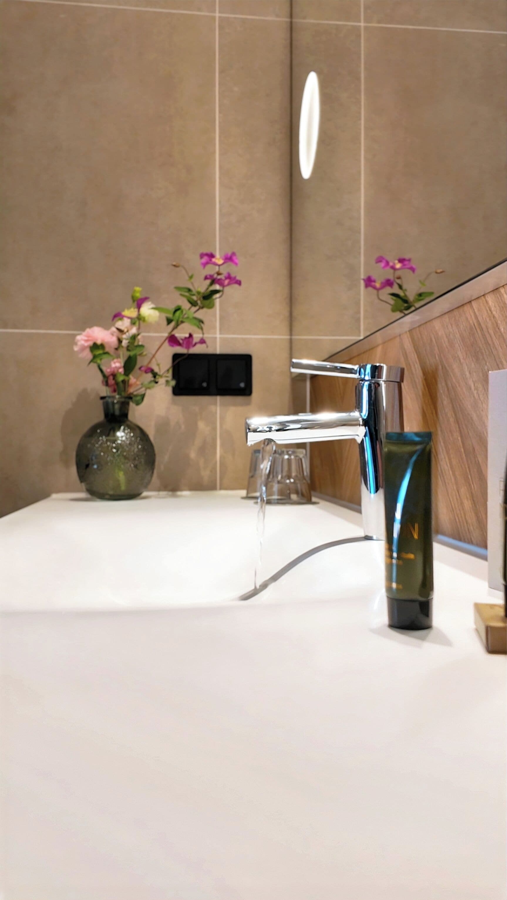 A modern bathroom with a chrome faucet, a glass vase with flowers, and a mirror.