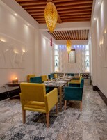 Uma área de jantar com uma mesa comprida posta para seis pessoas, rodeada por cadeiras amarelas e azul-esverdeadas.