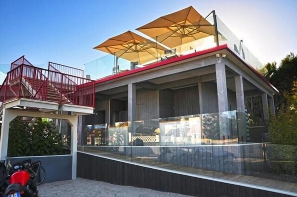 A modern outdoor seating area with a glass enclosure, red railings, and large umbrellas. - L'Angolo di Beppe (Porto Cesareo)