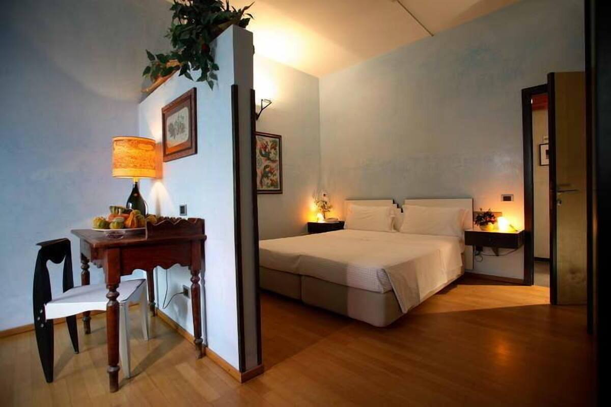 A bedroom with a bed, bedside table, lamp, and a small desk with a chair.